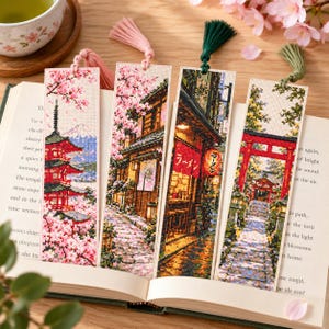 Könnte beinhalten: Vier rechteckige Kreuzstich-Lesezeichen mit japanisch inspirierten Motiven: eine rote Pagode mit Kirschblüten, ein Holzgebäude mit rosa Blüten, ein Ramen-Laden mit roten Laternen und ein roter Torii-Tor-Pfad, jeweils mit einer Quaste versehen.