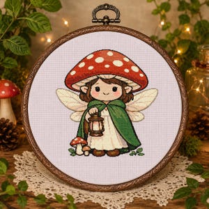 May include: A circular embroidery hoop containing a cross-stitch design of a fairy with brown hair, wearing a green cloak over a white dress, and a large red mushroom cap with white spots on their head. The fairy holds a small brown lantern.