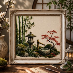 May include: A framed cross-stitch embroidery depicting a Japanese garden scene with green bamboo stalks, a stone lantern, a bamboo water fountain, a stone basin, and a red maple tree on a cream-colored fabric background, encased in a distressed white frame.