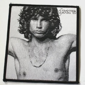 May include: A square embroidered patch featuring a black and white portrait of Jim Morrison with long curly hair. The image shows a shirtless figure with a thin necklace. The text The Doors is printed in the upper right corner with a black border.