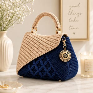 Peut inclure: Un sac à main structuré bicolore avec un rabat et une anse en crochet beige, ainsi qu'un corps en crochet bleu foncé orné d'un motif floral texturé. Une breloque circulaire dorée avec une icône de pelote de laine et le texte Toxunmatic est suspendue.