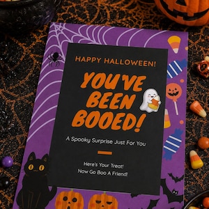 May include: A rectangular Halloween card with a purple border featuring spiderwebs, a black cat, and jack-o'-lanterns. The center black panel reads: HAPPY HALLOWEEN! YOU'VE BEEN BOOED! A Spooky Surprise Just For You. Here's Your Treat! Now Go Boo A Friend!