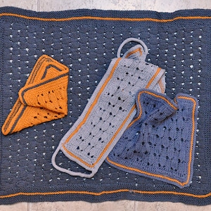 May include: Three crocheted squares in different patterns and colours. The largest square is blue with a white border and orange edging. The medium square is grey with a white border and orange edging. The smallest square is orange with a white border and blue edging.