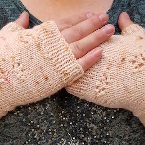 Puede incluir: Un par de guantes sin dedos de punto en color melocotón claro con un sutil patrón moteado. Los guantes tienen un delicado diseño de encaje.