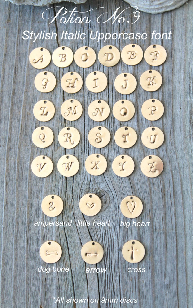 May include: Gold-colored metal charms with stylish italic uppercase letters A through Z, ampersand, hearts, dog bone, arrow, and cross. The charms are 9mm in diameter and are displayed on a wooden surface. The text "Potion No. 9" and "Stylish Italic Uppercase font" are also visible.