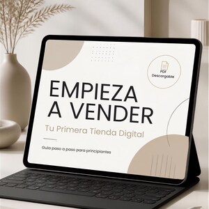 Puede incluir: Una tableta con teclado negro que muestra una guía digital titulada EMPIEZA A VENDER Tu Primera Tienda Digital Guía paso a paso para principiantes con un icono de PDF Descargable y elementos gráficos en beige sobre fondo blanco.