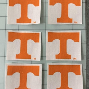 May include: Six individual square decals featuring a bold orange letter T logo on a white background. Each decal includes a small TM trademark symbol in the bottom right corner. The decals are arranged in two columns of three on a grid mat.