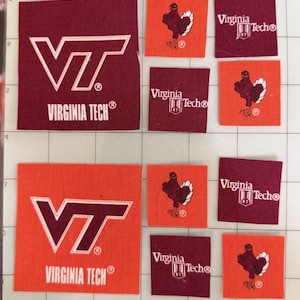 May include: A collection of fabric patches in maroon and orange featuring the Virginia Tech VT logo, the Virginia Tech text with the 1872 shield, and a turkey mascot graphic. The patches are arranged on a white grid surface with visible measurements.