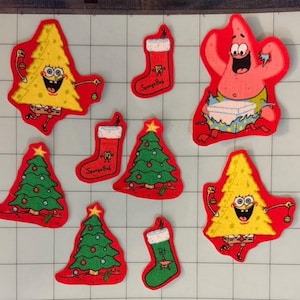 May include: A collection of felt patches featuring SpongeBob SquarePants as a Christmas tree, Patrick Star opening a gift, green Christmas trees with ornaments, and red or green stockings with the text SpongeBob or Pat embroidered on them.