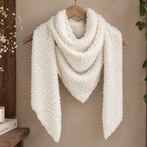May include: A cream-coloured triangular scarf with a textured, fuzzy knit pattern. The scarf is draped over a wooden hanger, featuring a pointed bottom edge and a soft, voluminous appearance created by the looped yarn construction throughout.