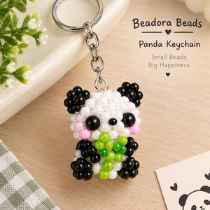 May include: A panda keyring crafted from small white, black, pink, and green beads, featuring a metal ring and chain. The text Beadora Beads Panda Keychain Small Beads Big Happiness is visible in the upper right corner of the image.