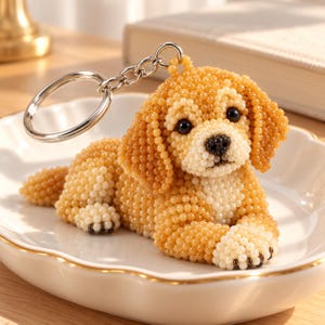 Pode incluir: Um porta-chaves com uma figura de cão tridimensional feita de pequenas contas redondas em tons de castanho-dourado e creme. O cão tem olhos e nariz de contas pretas, com um anel de metal prateado preso ao topo da cabeça.