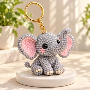 Può includere: Un portachiavi con una piccola figura di elefante realizzata con numerose minuscole perline grigie. L'elefante ha grandi orecchie con centri di perline rosa, occhi di perline nere e piccole perline color crema sui piedi. Un anello dorato è incluso.
