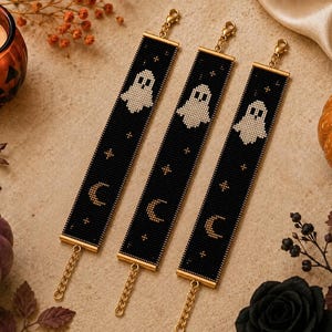 Puede incluir: Tres pulseras rectangulares de cuentas con fondo negro, motivos de fantasmas blancos y patrones de lunas crecientes y estrellas doradas. Cada pulsera incluye terminales de metal dorado, un cierre de mosquetón y una cadena ajustable.