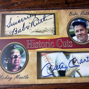 May include: A Historic Cuts trading card featuring portraits and signatures of Babe Ruth and Mickey Mantle. The card has a tan background with a maroon center stripe, displaying the text Babe Ruth, Mickey Mantle, and Historic Cuts in black.