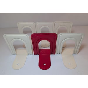 May include: A set of six metal bookends featuring an arched design with a ribbed border. Five of the bookends are off-white, and one is a deep red. Each piece has a flat base with a circular hole, and the metal construction provides a sturdy support.