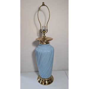 May include: A table lamp featuring a light blue ceramic base with a diagonal swirl pattern. The lamp includes a polished brass base, a matching brass neck, and a brass harp assembly at the top. The design is vertical and cylindrical in shape.