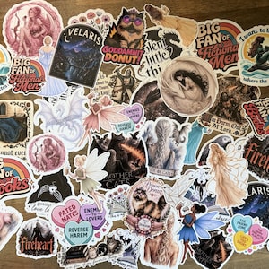 May include: A collection of assorted vinyl stickers featuring various illustrations, including fantasy characters, mythical creatures, animals, and text-based designs like Big Fan of Fictional Men, Velaris, and Fireheart, arranged in a dense, overlapping cluster.