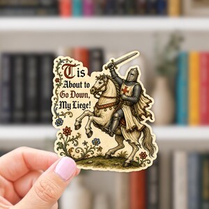 May include: A die-cut sticker featuring a medieval knight in armor riding a white horse, holding a sword aloft. The design includes floral vines and the text 'Tis About to Go Down, My Liege!' in a decorative, gothic-style font on a cream background.