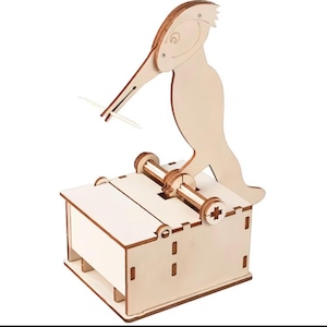 Può includere: Un distributore di stuzzicadenti in legno chiaro con una figura di uccello meccanica fissata su una scatola rettangolare. L'uccello ha un lungo becco progettato per trattenere uno stuzzicadenti, estratto dal vano interno quando l'uccello viene premuto verso il basso.