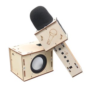 Può includere: Un set microfono e altoparlante in legno con una spugna antivento nera. La testa quadrata del microfono è incisa con un'icona di microfono e note musicali. La base rettangolare dell'altoparlante include un cono e pulsanti di controllo.