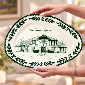 May include: An oval-shaped ceramic serving platter with a cream-coloured base and a dark green border featuring a leaf and flower pattern. The centre displays a dark green line drawing of a house with the text The First Home written above it.