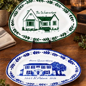Puede incluir: Dos platos ovalados de cerámica con bordes festoneados. El plato superior presenta una ilustración de una casa verde, el texto The Westredges y un borde de hojas verdes. El plato inferior presenta una casa azul, el texto Home Sweet Home y 1001 N Adams 2026.