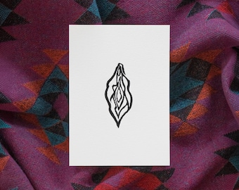 May include: A rectangular white card featuring a centered black ink line drawing of a vulva. The card is positioned against a purple fabric background that displays a repeating geometric pattern in shades of black, orange, and teal blue.