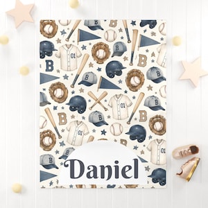 Op de afbeelding: Een rechthoekige deken met een herhalend patroon van honkbalillustraties, waaronder witte shirts met het nummer 01, bruine handschoenen, honkballen, knuppels, blauwe petten en wimpels. De naam Daniel is in donkerblauwe letters afgedrukt.