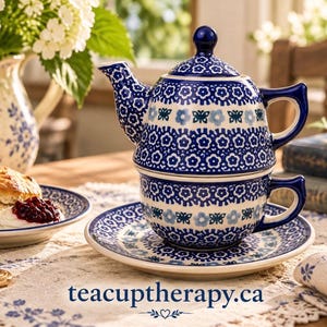 May include: A ceramic tea-for-one set comprising a teapot stacked on a teacup and saucer, adorned with a blue and white floral and butterfly pattern. The text teacuptherapy.ca is printed at the bottom centre of the image in blue lettering.