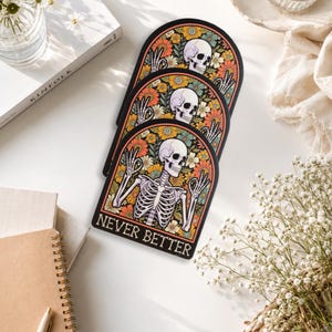 May include: Three identical arched stickers featuring a white skeleton making hand gestures against a background of orange, yellow, and teal flowers. The text "NEVER BETTER" is printed in a bold, serif font at the bottom of each sticker.