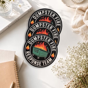 May include: Three circular embroidered patches featuring a green dumpster engulfed in orange and yellow flames. The black border contains the white text DUMPSTER FIRE RESPONSE TEAM arranged in a circular pattern around the central graphic.