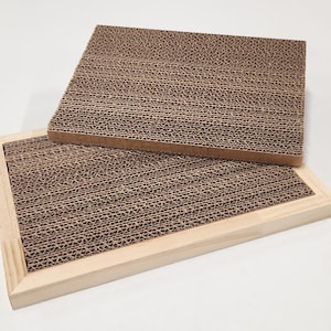 May include: A rectangular cat scratcher featuring a light-colored wooden frame and a replaceable corrugated cardboard insert. A second, separate rectangular corrugated cardboard insert is positioned diagonally on top of the framed base.