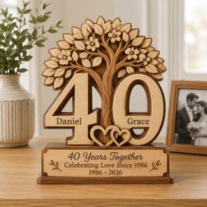 May include: A wooden decorative plaque featuring a carved tree with flowers above the number 40. The names Daniel and Grace are engraved on the digits. Two small hearts sit below, and the base reads 40 Years Together Celebrating Love Since 1986 1986-2026.