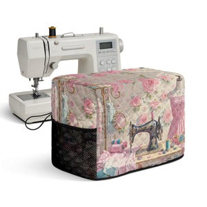May include: A white electronic sewing machine positioned behind a quilted fabric cover. The cover features a beige background with a pink rose pattern and a printed graphic of vintage sewing tools, including a sewing machine and spools of thread.