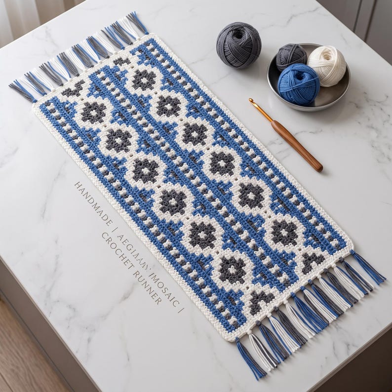 May include: A rectangular crochet runner featuring a geometric mosaic pattern in blue, white, and dark gray. The runner has fringe tassels on both ends in matching colors. Text on the runner reads HANDMADE | AEGEAN MOSAIC | CROCHET RUNNER.