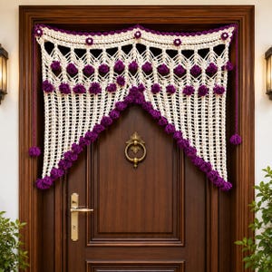 May include: A cream-colored crocheted door valance featuring a decorative scalloped edge and intricate lattice patterns. The valance is adorned with small purple pom-poms and tiny flower accents along the top border, with long purple tassels hanging from each side.