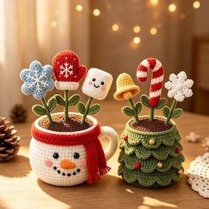 May include: Two crocheted holiday decorations: a white snowman mug with a red scarf containing a blue snowflake, red mitten, and marshmallow, and a green tiered Christmas tree pot holding a yellow bell, candy cane, and white snowflake.