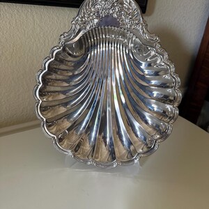 Plat de service vintage en forme de coquille Saint-Jacques, plaqué argent, orné de motifs floraux et de volutes sur le dessus, ressemblant fortement à des modèles existants.