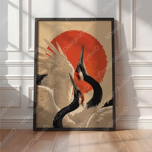 以下が含まれることがあります： ベージュの背景に、黒い首と赤い冠を持つ2羽の白い鶴が、大きな赤い円形の太陽の前に描かれた額装アートプリント。鳥は翼を部分的に広げ、頭を傾けた姿で表現されており、全体が黒いフレームに収められている。