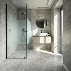 Puede incluir: Un baño con azulejos de pared y suelo con patrón de mármol gris, una cabina de ducha de cristal con un panel central esmerilado, un mueble de lavabo suspendido con un lavabo blanco y un espejo circular sobre el lavabo.