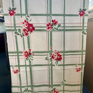 May include: A rectangular fabric cloth featuring a white background with a grid pattern of sage green stripes and thin red lines. The cloth is decorated with scattered clusters of pink and red flowers with green leaves throughout the design.