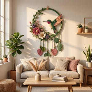 May include: A circular wall hanging featuring a crocheted green hummingbird in flight, surrounded by a wreath of crocheted flowers and leaves in shades of pink, purple, and white, with dangling leaf-shaped accents and wooden beads.