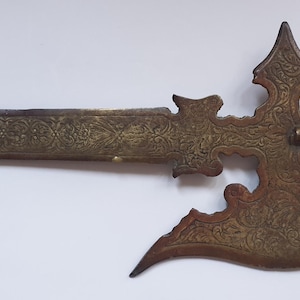 May include: A bronze-toned metal halberd featuring an elongated blade and a curved axe head. The entire surface is covered in intricate, etched floral scrollwork patterns. A cylindrical handle section with raised bands is attached to the base.
