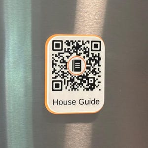 May include: A rectangular magnet with rounded corners featuring a black and white QR code on a white background. The center of the QR code displays an orange circular icon of a book. The text House Guide is printed in black below the code.
