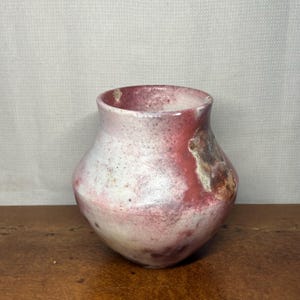 May include: A ceramic vase with a rounded body and a wide opening, featuring a mottled surface with blended shades of white, soft pink, and deep reddish-brown. The texture appears matte with subtle variations in colour intensity across the exterior.