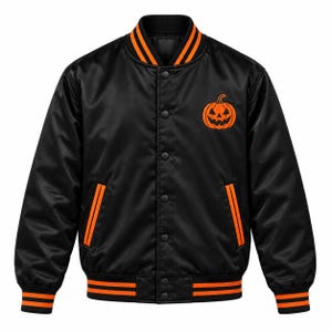 Puede incluir: Una chaqueta universitaria de satén negro con una calabaza de Halloween naranja bordada en el pecho izquierdo. La chaqueta cuenta con cierre de botones a presión, dos bolsillos laterales con ribete naranja y puños, cuello y bajo acanalados.