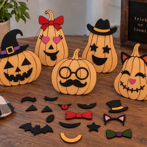 May include: Five light orange wooden pumpkin cutouts with various facial expressions and accessories, including hats, bows, and glasses. Below the pumpkins are several loose, interchangeable wooden facial features and accessories in black, red, and green.
