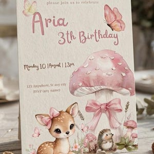 Pode incluir: Um cartão de convite de aniversário com uma ilustração em aguarela de um cervo com um laço cor-de-rosa, um cogumelo cor-de-rosa grande com um laço e um ouriço. O texto diz: please join us to celebrate Aria 3th Birthday, Monday 10 August 13pm, 123 Anywhere, St any city, RSVP (any name).