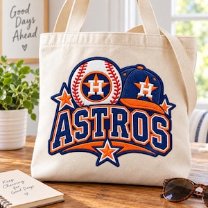 May include: A cream-colored canvas tote bag featuring an embroidered Houston Astros logo. The design includes a baseball, a blue and orange baseball cap, and the word ASTROS in bold blue and orange lettering, accented with orange stars.